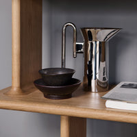 Stylish black bowls and a sleek silver pitcher on a natural wood shelf, featuring minimalist design and elegant contrast.