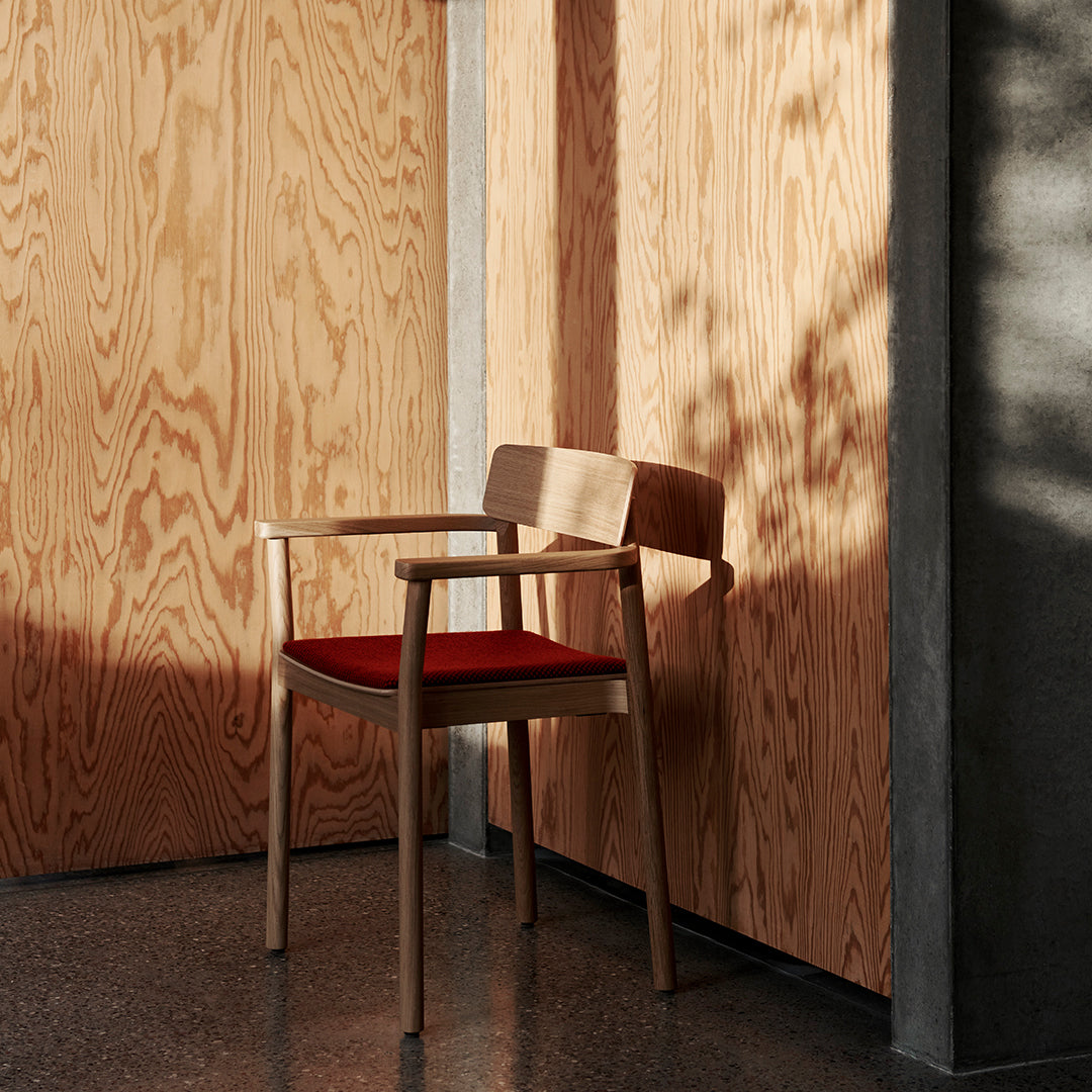 "Wooden chair with a rich red cushion against a backdrop of light oak and gray concrete."