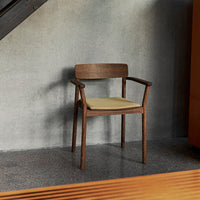 Wooden chair with a warm brown finish and a soft yellow cushion, set against a textured gray background.
