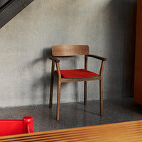 Wooden chair with a rich brown finish and a vibrant red cushion, set against a textured gray background.