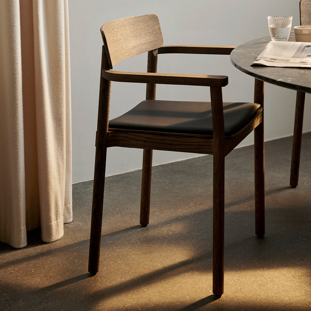Wooden chair with a walnut finish and black leather seat, featuring a minimalist design against a neutral backdrop.