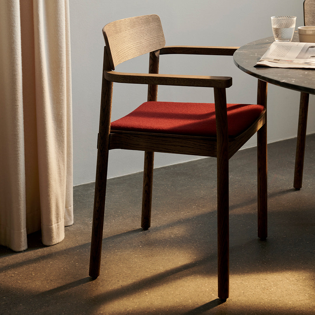 Wooden chair with rich brown frame and vibrant red cushion, set against a neutral backdrop.