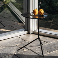 Black metal side table with a textured top, featuring a minimalist design, set against a light stone floor.