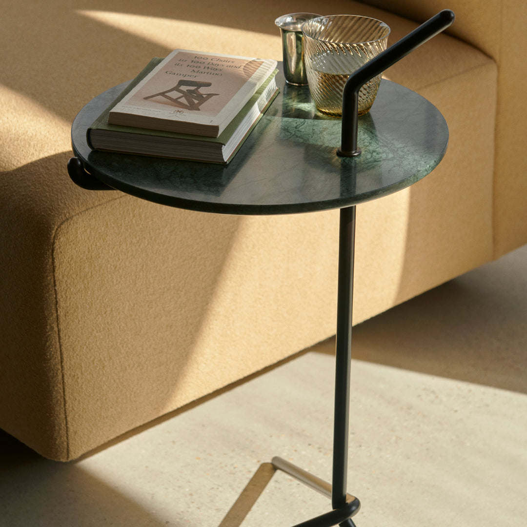 Round green glass tabletop with a matte black metal base, set against a neutral beige couch. Clean, modern aesthetic.