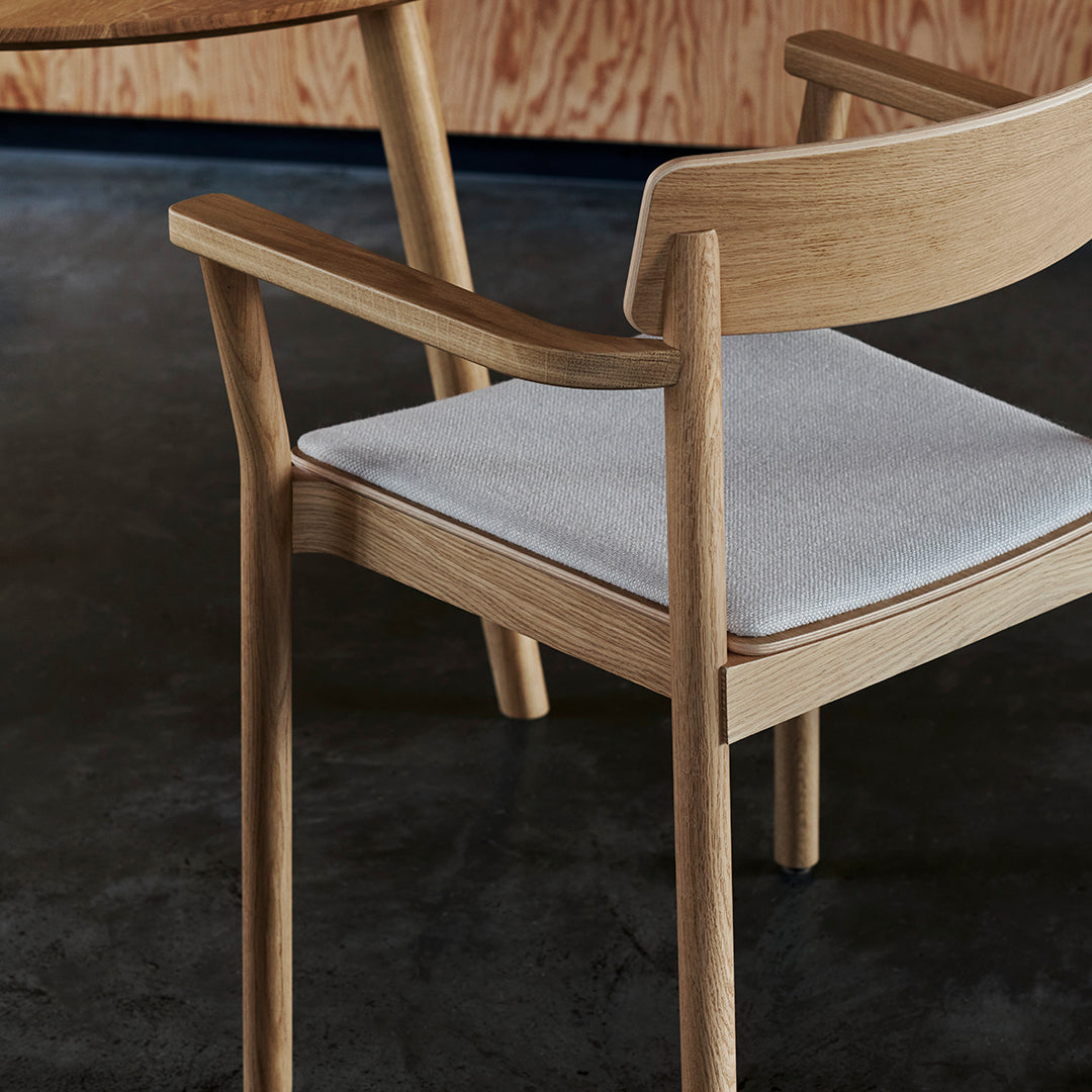 Light wood chair with a smooth, beige fabric cushion against a dark, textured floor. Modern and minimalist design.