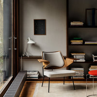 Modern armchair featuring a beige seat and walnut wood accents against a neutral backdrop with books and a pop of red.