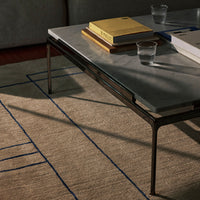 Modern coffee table with a sleek gray marble top and geometric patterns on a neutral-toned rug with blue accents.