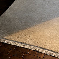 Beige textured rug with subtle fringed edges, complementing dark brown flooring. Perfect for cozy interiors.