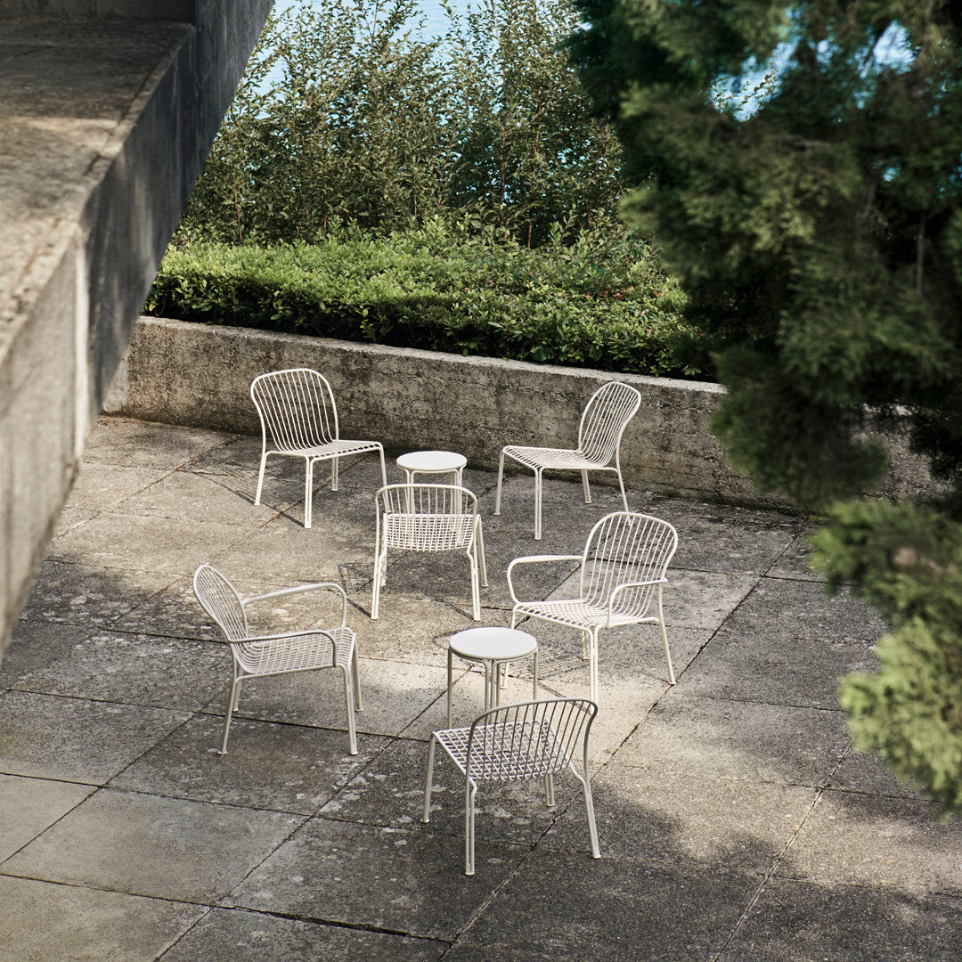 Set of white woven outdoor chairs and table against a natural green backdrop, featuring a minimalistic design.