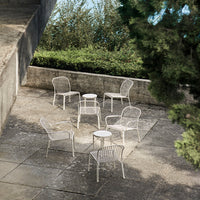 Set of white woven outdoor chairs and table against a natural green backdrop, featuring a minimalistic design.