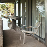 White metal chair with a minimalist design, featuring a sleek pattern, set against a serene outdoor backdrop.
