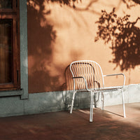 "White metal chair against a textured orange wall, with soft shadows creating a play of light and pattern."