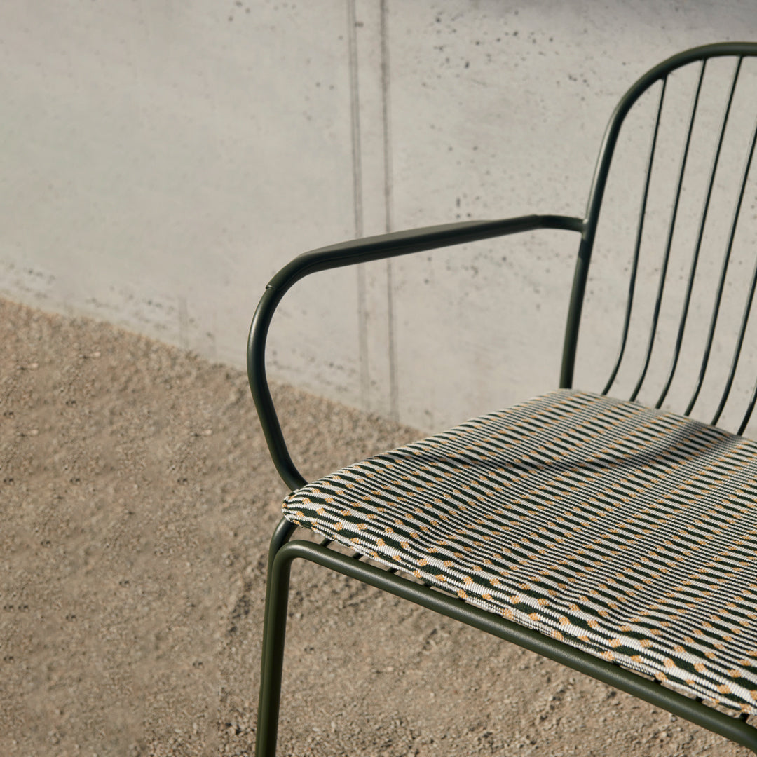 Black and white striped seat pattern on a green metal chair against a neutral concrete background.