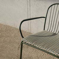 Black and white striped seat pattern on a green metal chair against a neutral concrete background.