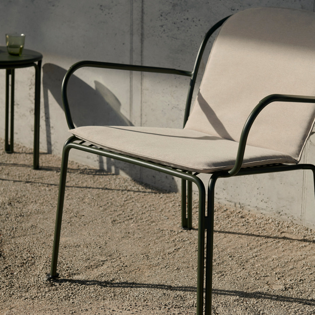 Beige cushioned chair with a sleek black metal frame, set on a textured gravel surface.