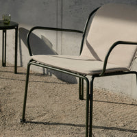 Beige cushioned chair with a sleek black metal frame, set on a textured gravel surface.