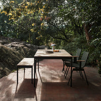 Modern outdoor dining set featuring a natural wood table with black metal accents and green patterned chairs in a serene garden setting.