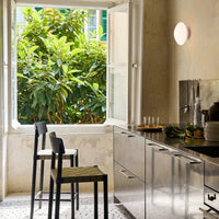 "Modern kitchen with stainless steel accents, green plants outside, and black chairs with textured olive-green seats."