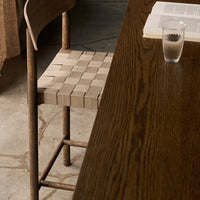 "Natural wood chair with a beige woven seat, paired with a dark wooden table and textured gray floor."