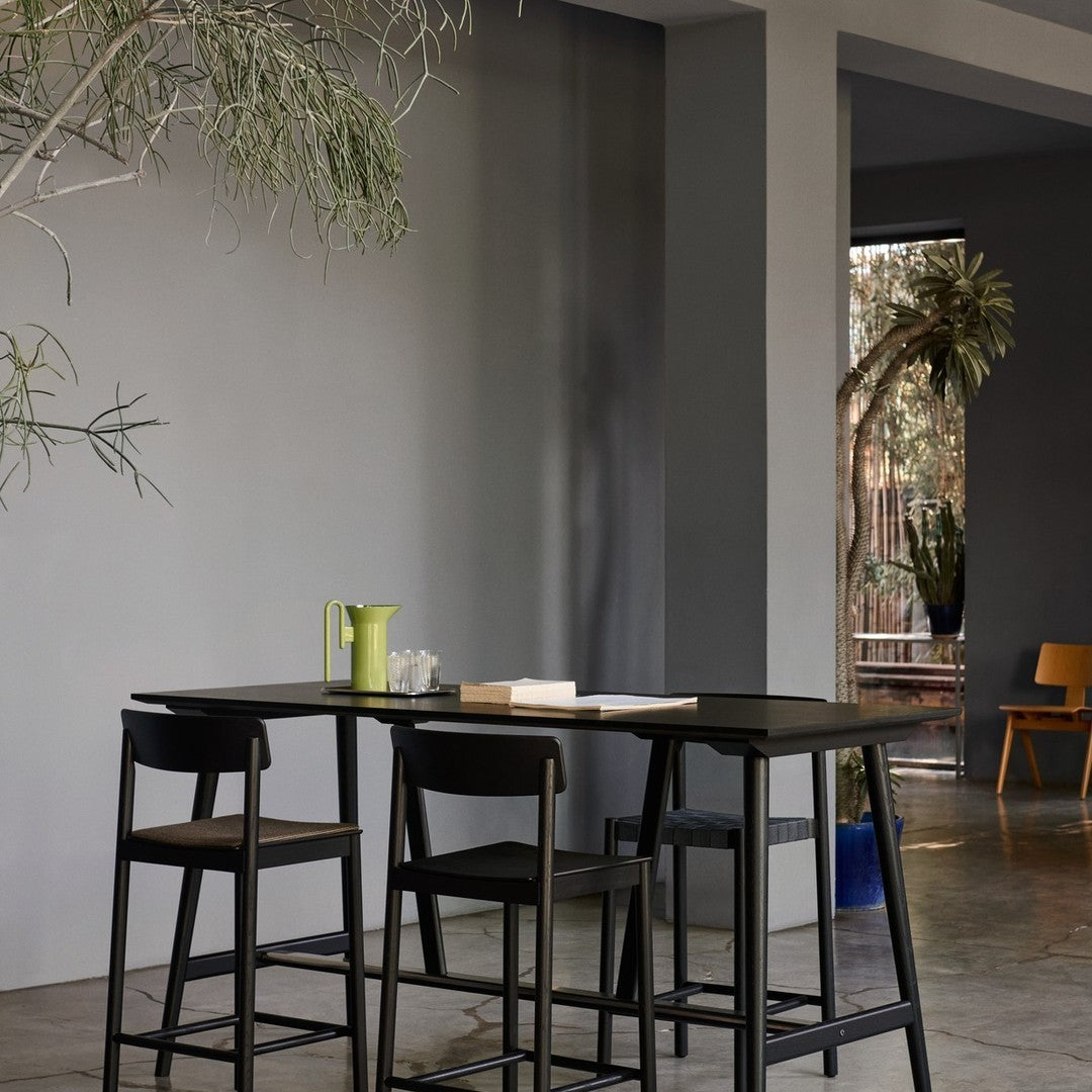 Black bar stools, sleek black table, vibrant green pitcher, neutral gray walls, and earthy tones create a modern look.