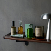 "Stylish shelf featuring green and amber glass bottles with neutral labels on a wooden surface against a gray background."