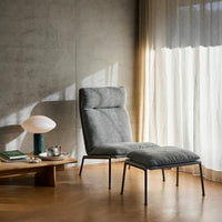 Gray upholstered chair with a matching ottoman, set against a neutral backdrop of light wood and soft, flowing curtains.