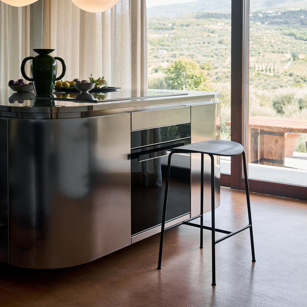 Sleek stainless steel kitchen island with a black metal stool against a warm, earthy backdrop. Modern and minimalist design.