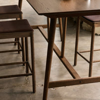 Dark wood table with light grain, complemented by brown patterned seat cushions on rustic wooden stools.