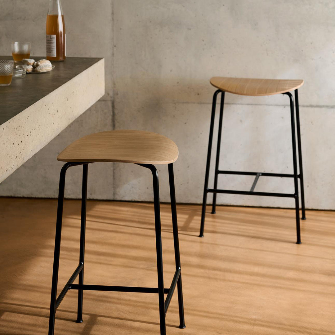 Natural wood finish bar stools with sleek black metal legs, set against a neutral concrete backdrop.