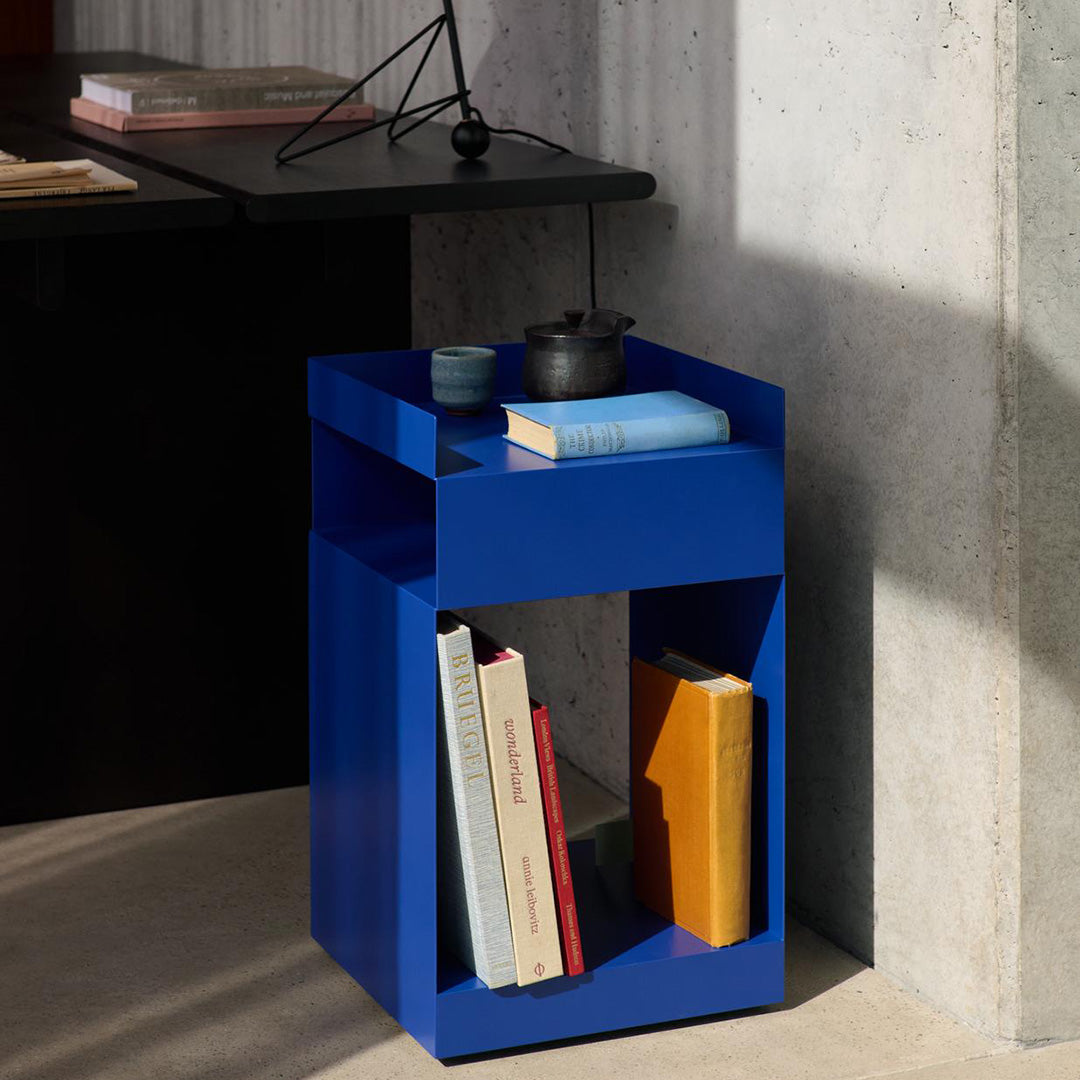 Vibrant blue cube side table with geometric design, showcasing books in yellow and white. Modern minimalism aesthetic.