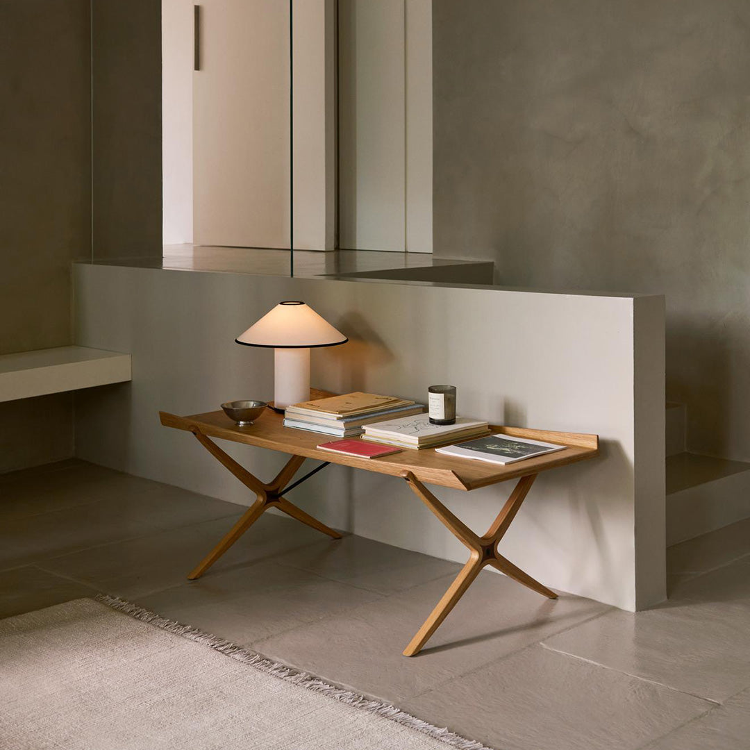 Light wood table with crossed legs, complemented by earthy tones and soft lighting in a minimalist interior setting.