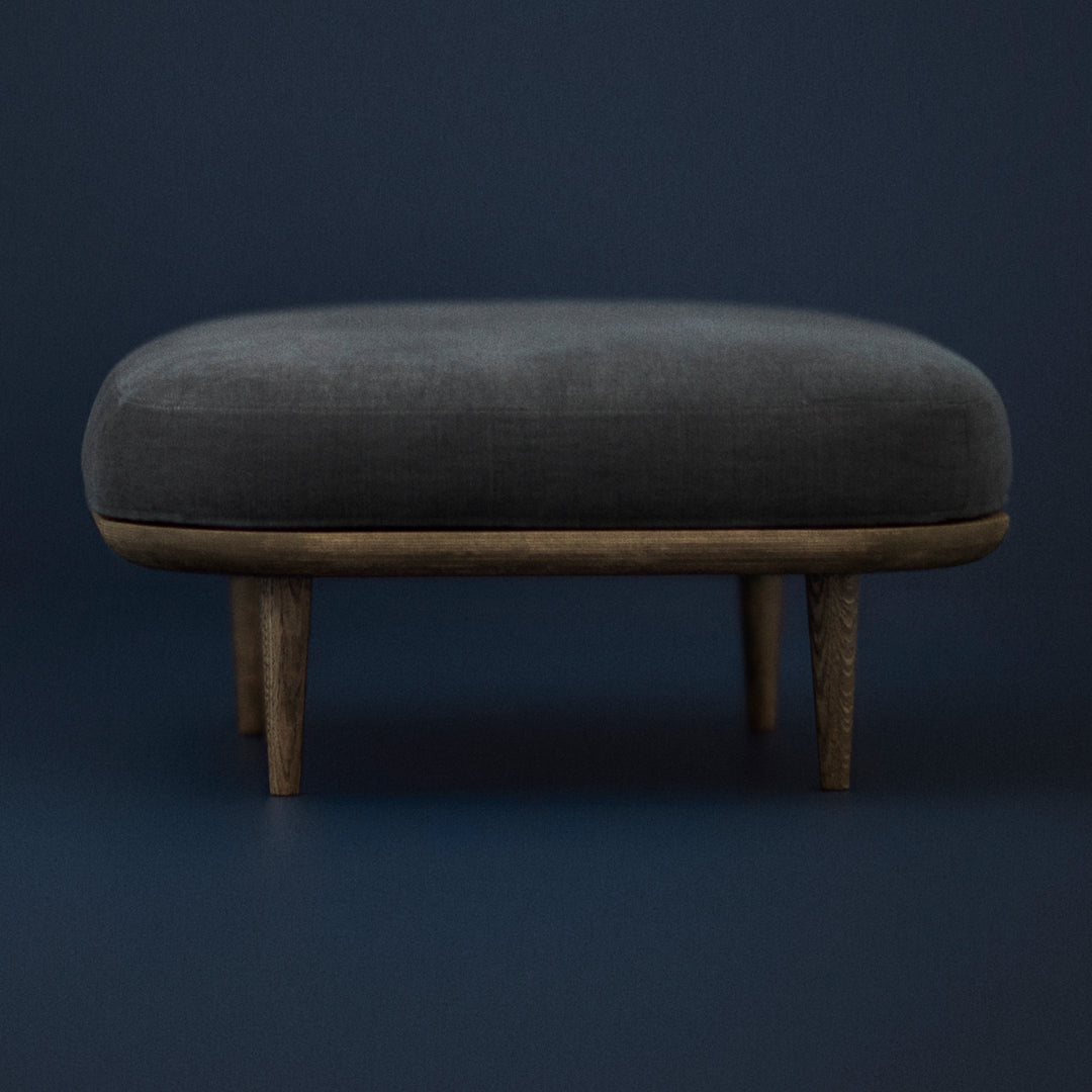 Dark gray upholstered ottoman with natural wood legs against a deep blue background. Smooth finish and modern design.