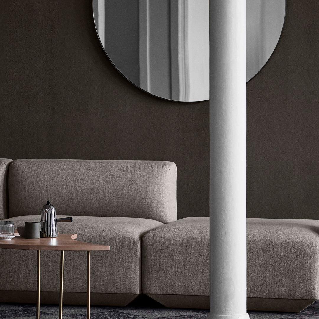 "Modern gray fabric sofa with clean lines, complemented by a round mirror and a neutral wall backdrop."
