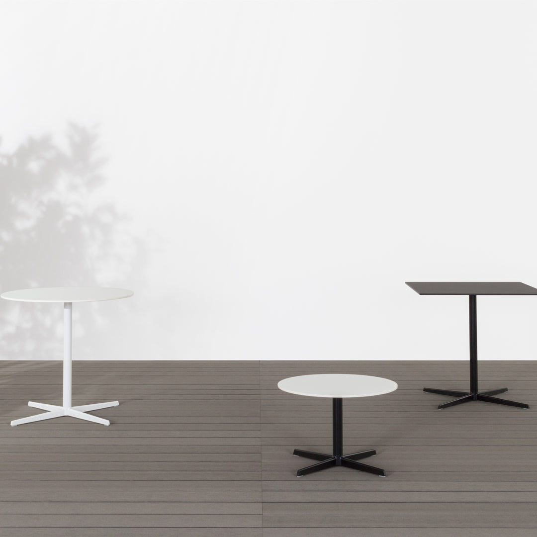 Set of three modern tables in white and black, featuring sleek designs and smooth finishes on a wooden floor.