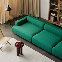 Emerald green modular sofa with clean lines on a neutral rug, complemented by earthy accent table and soft curtains.