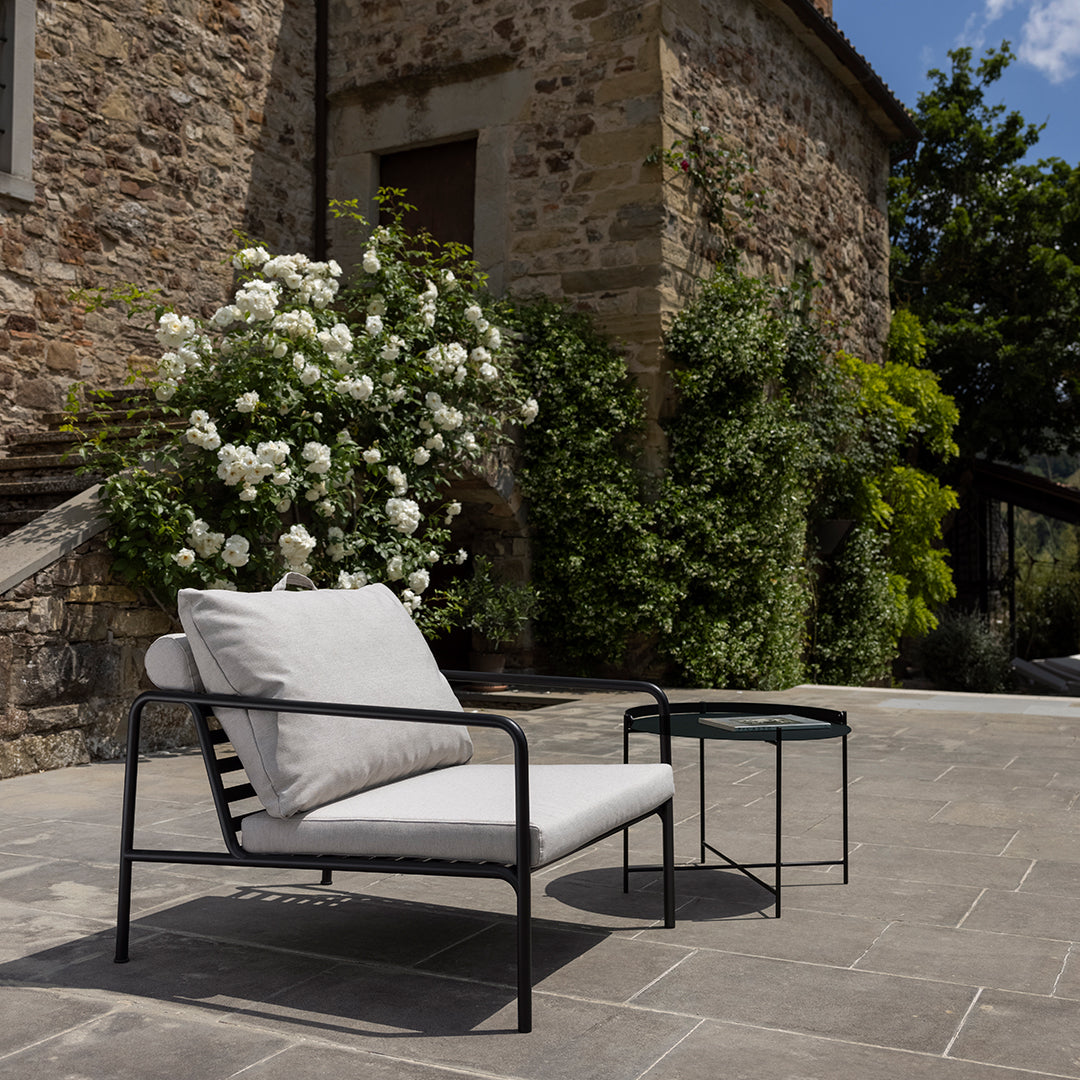Stylish white cushioned outdoor chair with black metal frame, set against a stone wall and lush green plants.