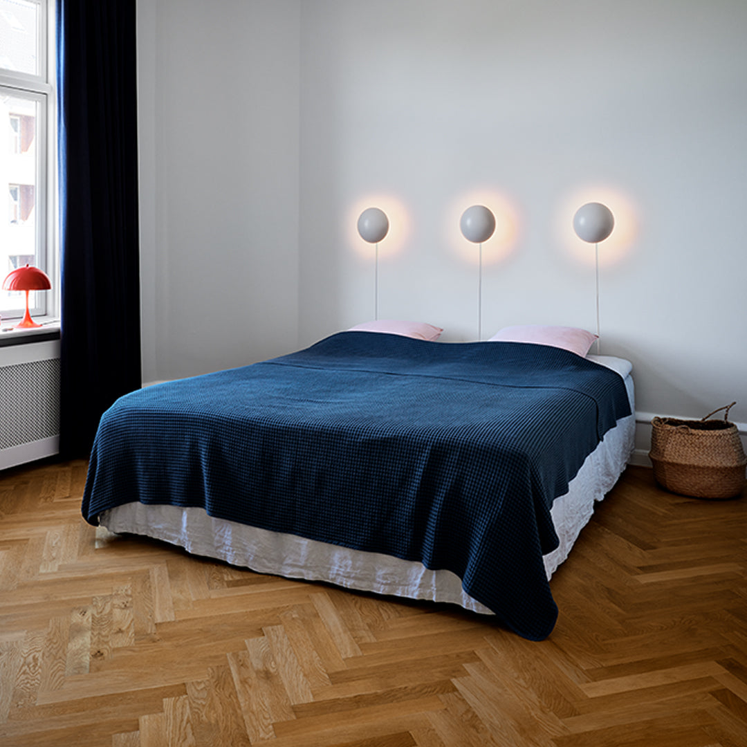 Navy blue bedspread with a smooth texture, complemented by warm lighting and neutral-toned bedding in a modern bedroom setting.