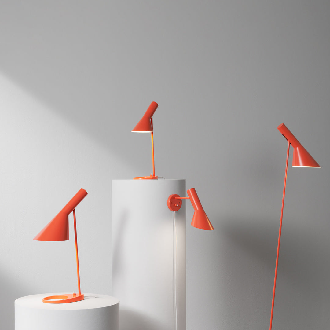 Three modern orange lamps with sleek designs on white pedestals against a neutral background.