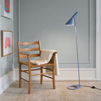 Light blue floor lamp beside a natural wood chair with a cream throw, against a soft gray wall.