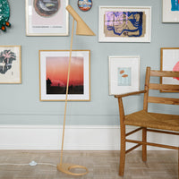 Modern wooden floor lamp with a sleek design, featuring a natural wood finish against a pastel blue wall.