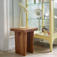 Brown wooden side table with a smooth finish, complemented by a modern cream lamp against a light backdrop.