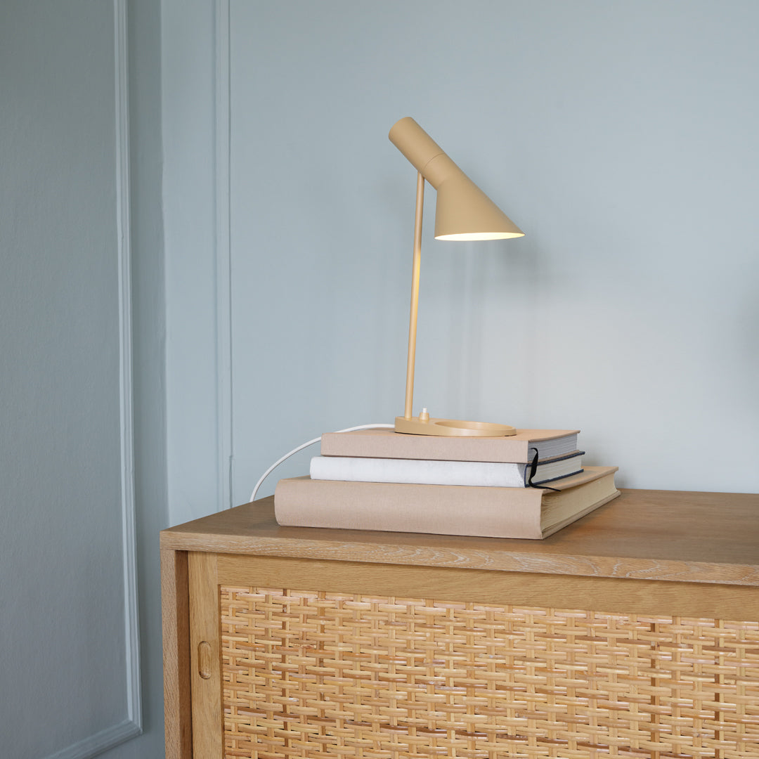 Minimalist beige lamp atop stacked light-colored books on a natural wood cabinet with woven texture.