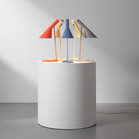 Colorful table lamps in orange, blue, gray, and yellow, arranged on a minimalist white cylindrical table.
