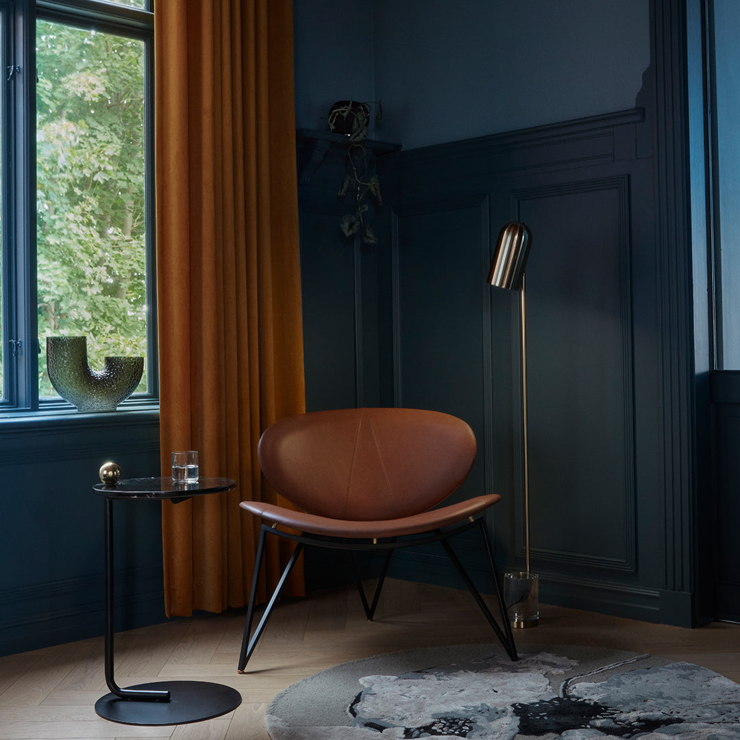 Brown leather chair with black legs, yellow curtains, blue walls, and a gray rug, creating a modern interior aesthetic.
