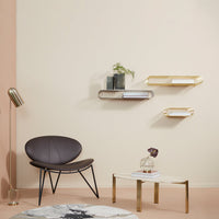 Modern interior featuring a beige wall, black chair, gold shelves, and a marble-patterned coffee table.
