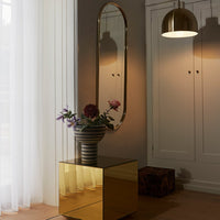 "Gold mirrored cube table with bold striped vase and vibrant flowers against soft white curtains."