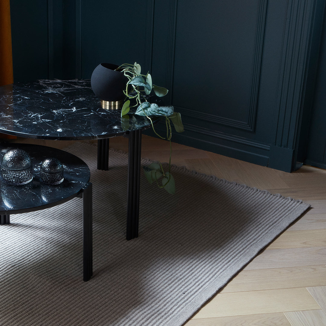 Black marble table with smooth surface, surrounded by a textured beige rug and dark green walls.