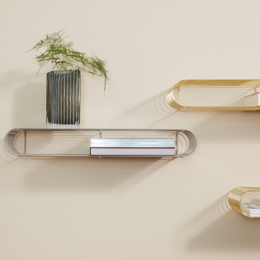 "Wall-mounted shelves in metallic gold and silver with a textured black vase and green plant against a neutral background."
