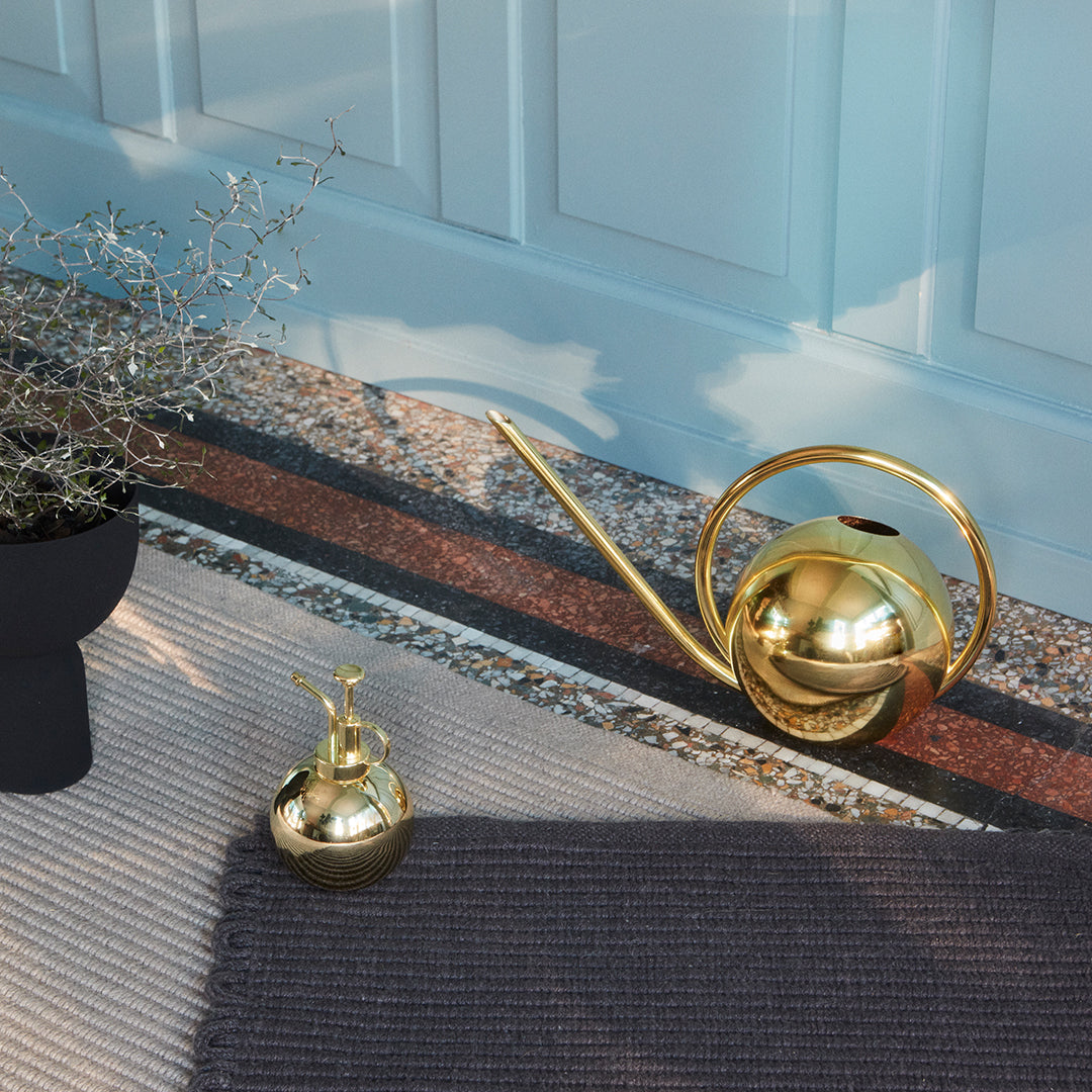 Gold watering can and small vase on a textured rug, featuring muted tones and geometric patterns. Perfect for decor.