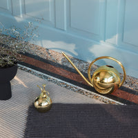 Gold watering can and small vase on a textured rug, featuring muted tones and geometric patterns. Perfect for decor.
